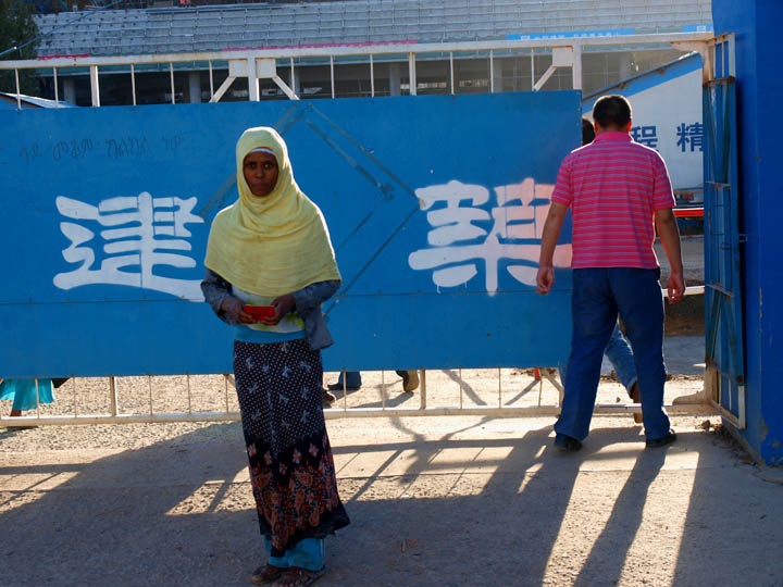 An Ogadeni woman exits the Chinese government's construction of the new African Union complex on April 13, 2011. Just after I took this photo the Chinese man in the pink shirt ordered an Ethiopian security guard at the site to wrest my camera from me because he deemed it forbidden to take photos of the Chinese foremen and engineers. ©2011 Derek Henry Flood
